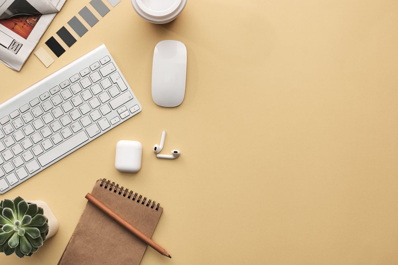 A minimalist workspace flat lay with keyboard, mouse, notebook, and succulent on a beige background.